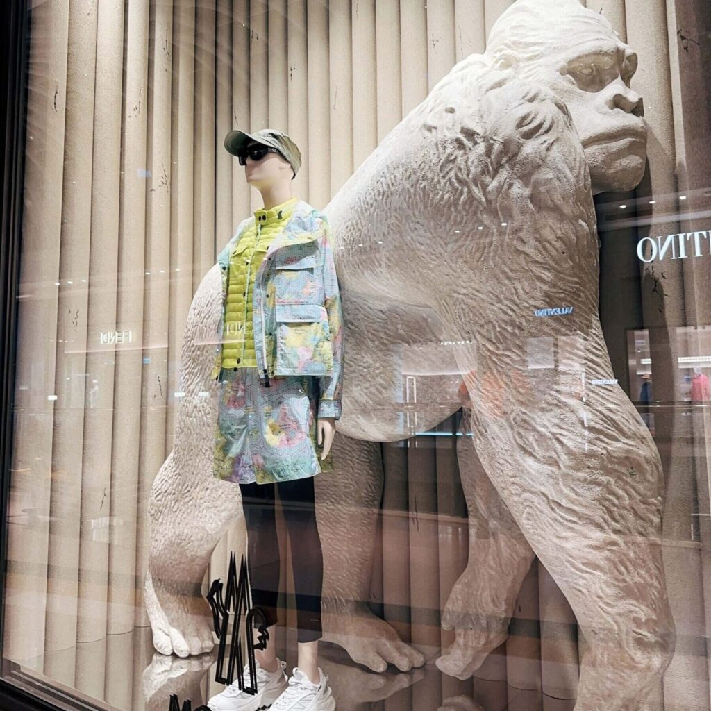 Mannequin in colorful outfit beside large gorilla sculpture in store display window.