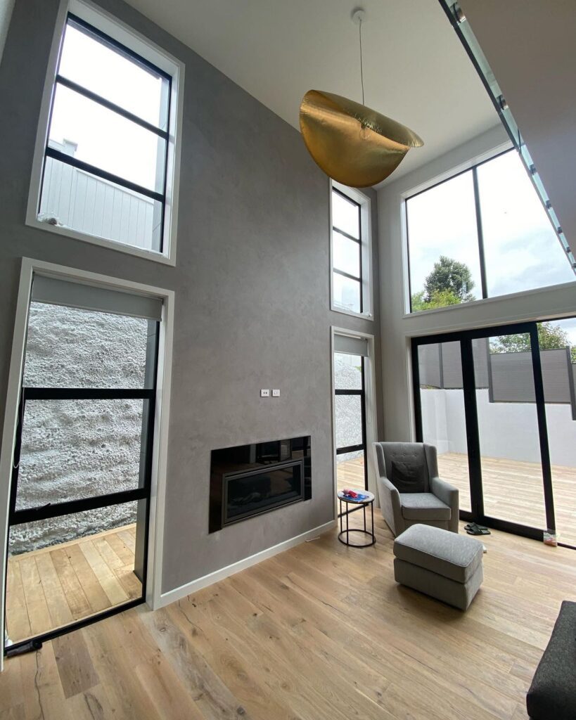 Modern living room with large windows, textured walls, and wooden flooring.