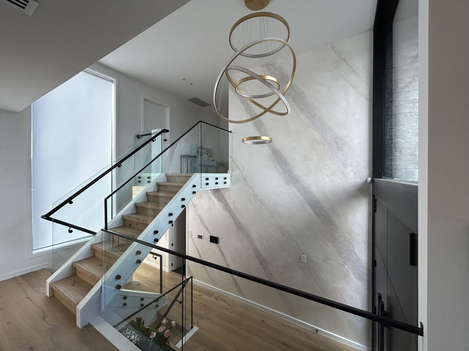Modern staircase with glass railing and textured wall in a well-lit interior space.