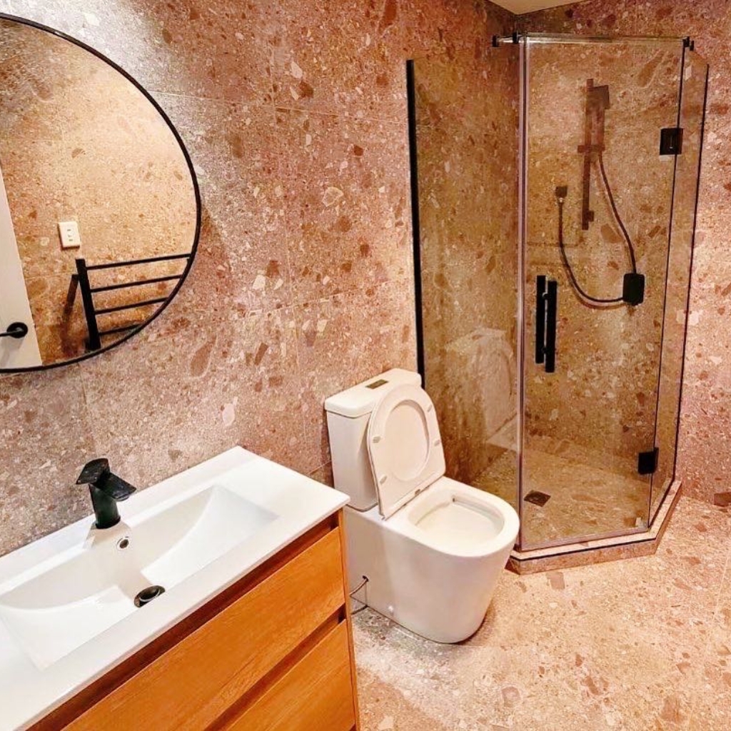 Modern bathroom with round mirror, glass shower, and wooden vanity.