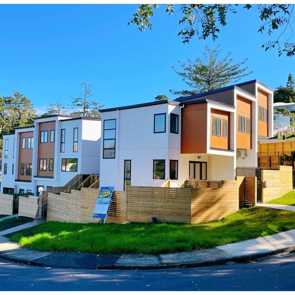 Modern townhouses with wooden fences and green lawns on a sunny day.