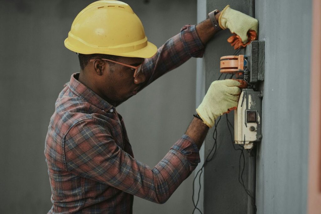 Person in hard hat performing electrical maintenance on a wall.