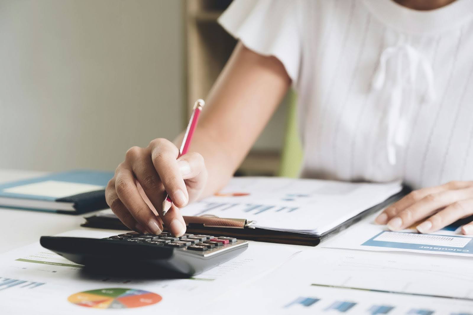 Person calculating expenses with a calculator and documents on a desk.