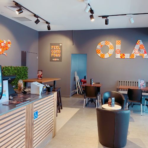 Modern cafe interior with seating, counter, and decorative wall art spelling "OLA."