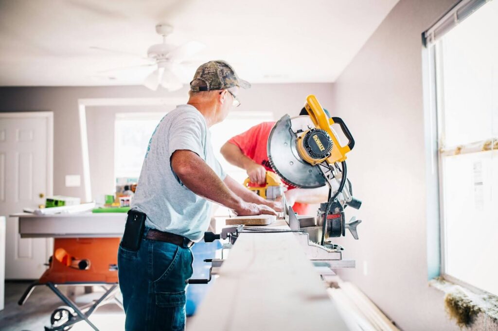 Two men working with a circular saw in a bright room.