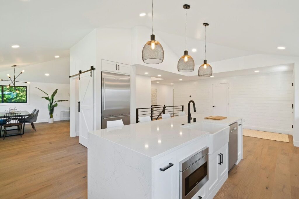 Modern kitchen with white island, pendant lights, and dining area in background.