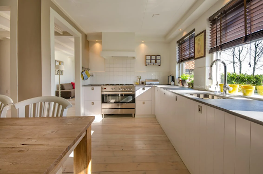 Modern kitchen with wooden floors, white cabinets, and large windows.