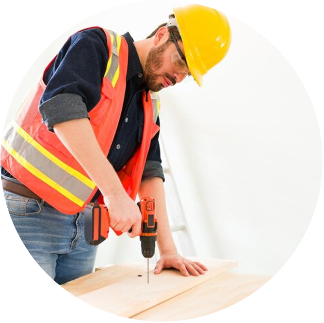 Man in safety gear using a drill on wooden surface.